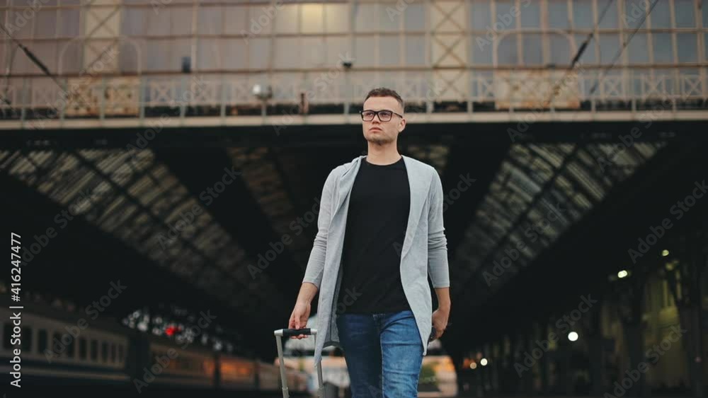 A man is walking along with the station platform. He's holding a suitcase. 4K.