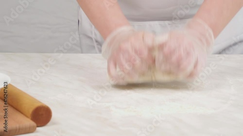 Female hands in gloves knead dough on the table.