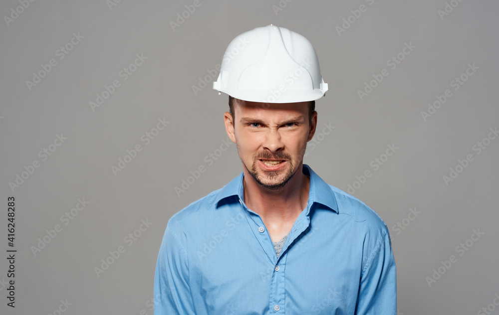 Architect in a white helmet and in a blue shirt on a gray background emotions portrait