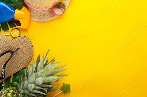 Summer background with straw hat, beach slippers, pineapple and slippers yellow background, copy space.