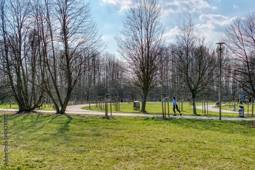 ćwiczenia w parku na przedwiośniu, drzewa bez liści a trawa soczyście zielona, wrotkarka jedzie ścieżką parkową © Jarek Witkowski