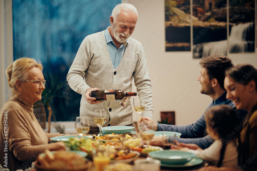 Happy mature man serving wine during family lunch in dining room. Happy mature man serving wine during family lunch in dining room.