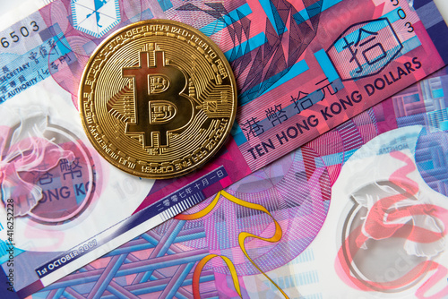 Photography Golden Bitcoin Cryptocurrency coin on Hong Kong Dollar banknotes.