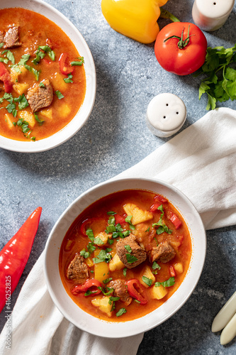 goulash is a traditional Hungarian dish with beef, potatoes, tomatoes and peppers. goulash in white plates with vegetables for cooking