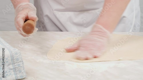 The cook rolls out thin dough with a wooden dough roller on the table with flour.
