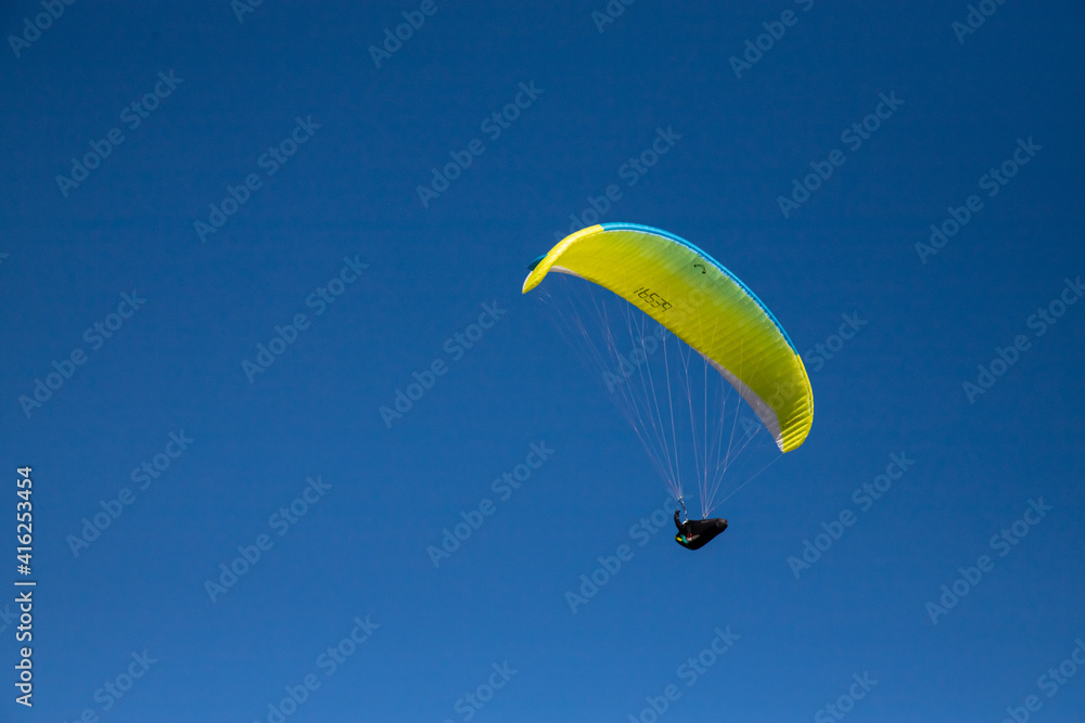 gelber gleitschirm unter blauem Himmel, Pilot in Wärmesack im Gleitflug bei sonnigem Frühling nahe gelber gleitschirm unter blauem Himmel, Pilot in Wärmesack im Gleitflug bei sonnigem Frühling nahe