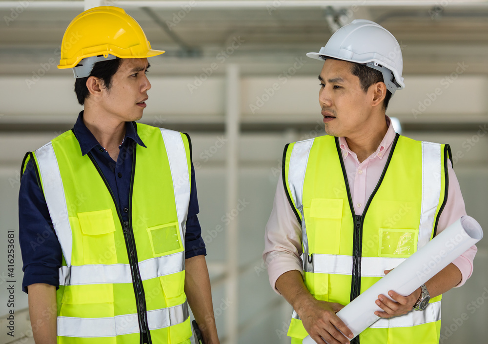Portrait of young and handsome two Asian male engineers in yellow protective vest working and taking with intimated gesture in factory Portrait of young and handsome two Asian male engineers in yellow protective vest working and taking with intimated gesture in factory