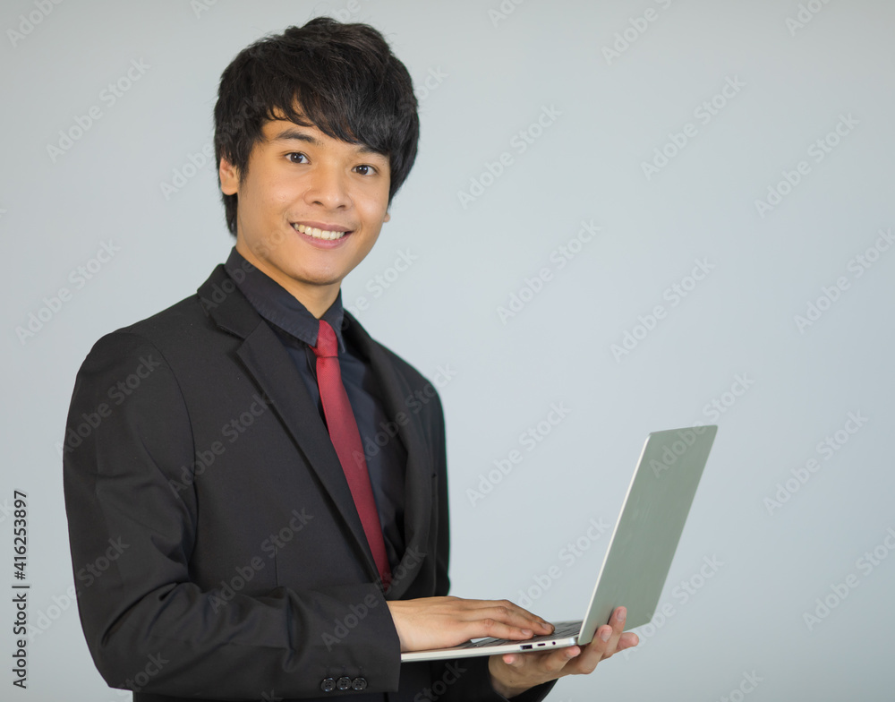 Cute and handsome Asian businessman executive look in formal suit standing and holding laptop notebook computer Cute and handsome Asian businessman executive look in formal suit standing and holding laptop notebook computer