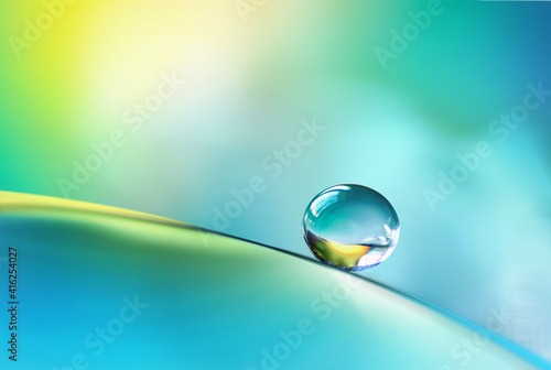 Beautiful clean transparent bright drop of water on smooth surface in blue and yellow colors, macro. Creative image of beauty of environment and nature. © Laura Pashkevich