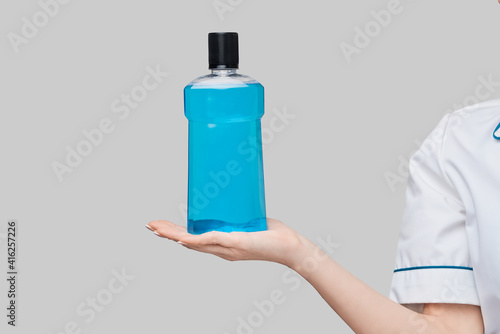 Foto woman dentist doctor holding bottle of mouthwash standing over grey background