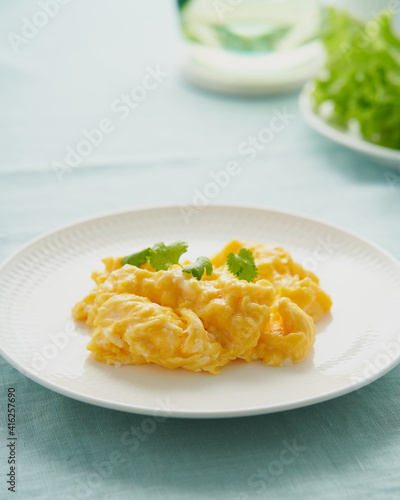 Scrambled eggs, omelette. Breakfast with pan-fried eggs. Texture of omelet on white plate on green mint linen textile tablecloth. Keto ketogenic diet. Soft light, side view, vertical