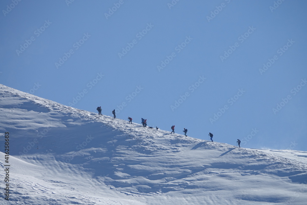 Climb a mountain. A group of hikers climbs the snow-capped peak of Mt. Hiking group in winter snowy mountains. Climbers walking on climbing the mountain range.