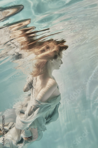 A girl in an airy light dress swims underwater as if flying in zero gravity