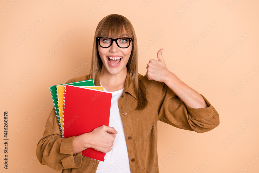 Photo of charming happy young woman make thumb-up hold notes isolated on pastel beige color background Photo of charming happy young woman make thumb-up hold notes isolated on pastel beige color background