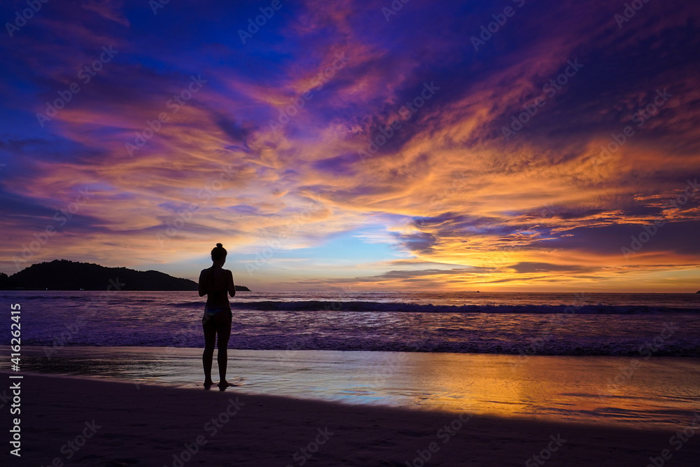 Beautiful sunset on the beach, dark silhouette of a girl against the background of the sunset