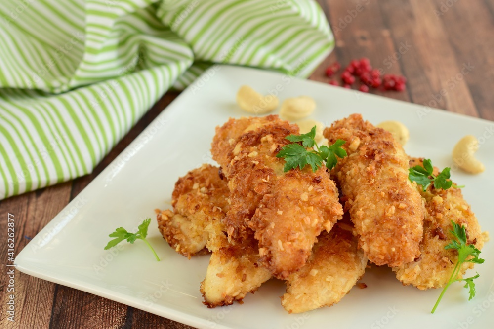Chicken fingers or chicken strips breaded with cashew and coconut flakes garnish with parsley Chicken fingers or chicken strips breaded with cashew and coconut flakes garnish with parsley