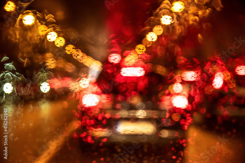 Night city life trough windshield on rainy day. Blurred cars, lights and raindrops. Colorful background. Closeup.