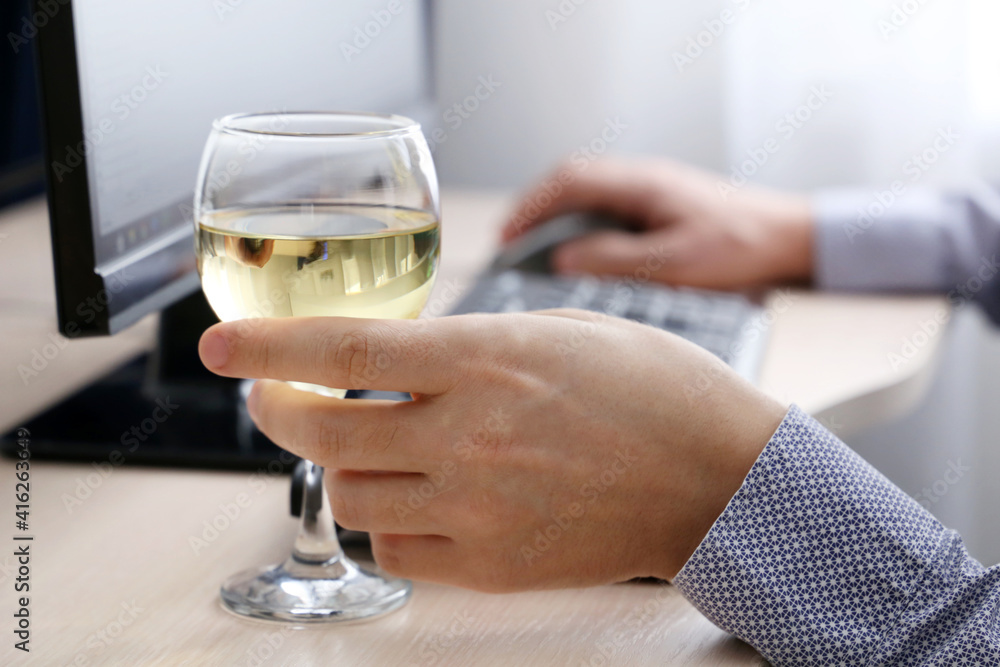 Glass of white wine in male hand, man drinking alcohol sitting at PC keyboard. Remote work at home or relax at office Glass of white wine in male hand, man drinking alcohol sitting at PC keyboard. Remote work at home or relax at office