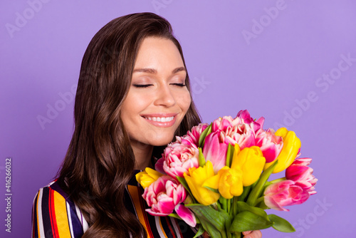 Photo portrait of happy woman smelling aroma of tulips flowers bunch smiling isolated vibrant violet color background