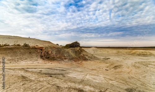 Sandy plain and a man in the background against the background of the forest and the blue sky with clouds