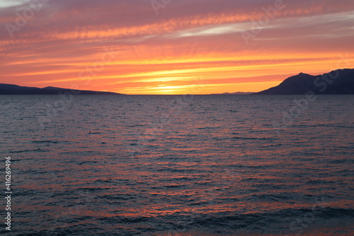 Bright red orange sunset on the Adriatic coast  bright clouds and sun rays are reflected on the sea surface