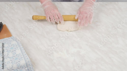 Close-up, female hands in gloves crumple the dough and roll it out with a dough roller