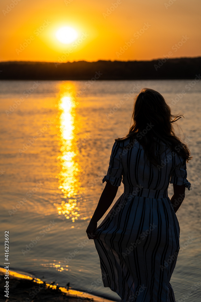 Fototapeta premium Woman standing at the beach on sunset in dress