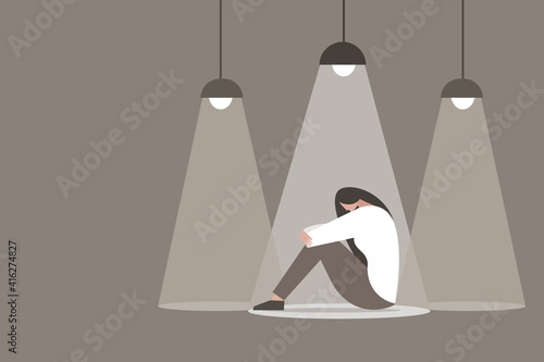 A depressed girl sitting in the dark with spot light falling on her photo