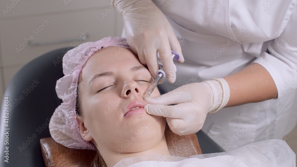Cosmetologist in a protective medical gloves doing injections to woman's lips. Bio revitalization procedure. Young woman getting beauty facial injections in salon. Lip reshaping in cosmetology