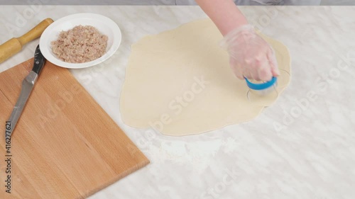 A woman's hand in a glove cuts circles out of thin raw dough. Preparation for dumplings.