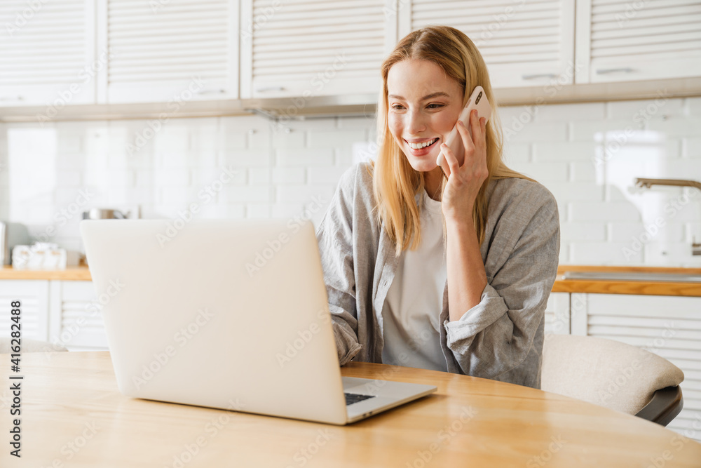Joyful blonde girl using laptop and talking on smartphone Joyful blonde girl using laptop and talking on smartphone