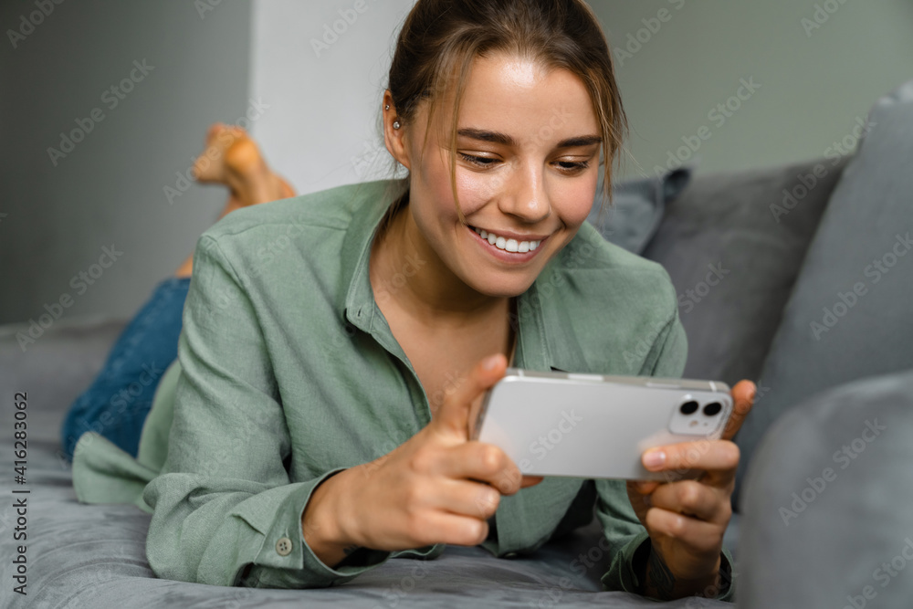 Happy nice woman using mobile phone while lying on sofa Happy nice woman using mobile phone while lying on sofa