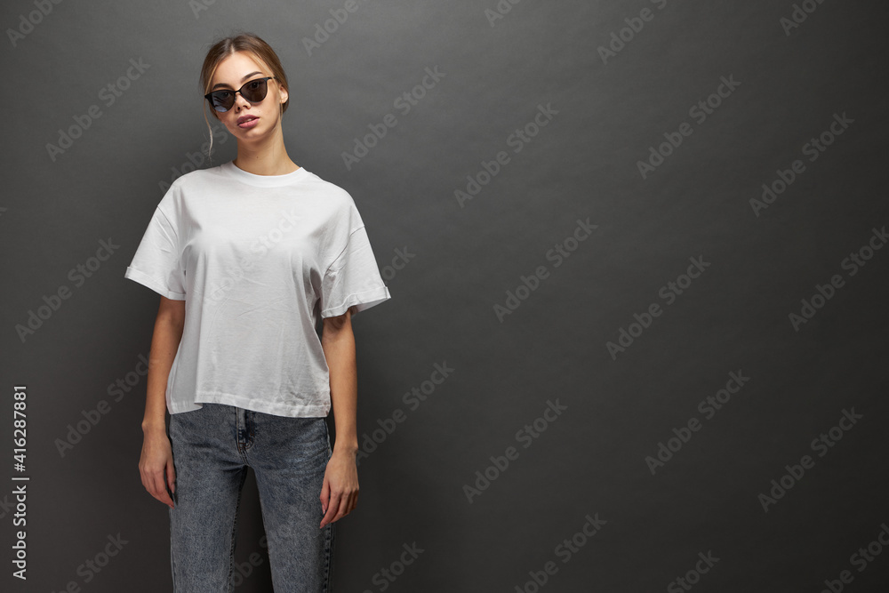 Woman wearing white blank t-shirt with space for your logo, mock up or design over gray background Woman wearing white blank t-shirt with space for your logo, mock up or design over gray background