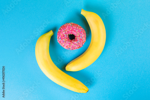 Nutrition. Two bananas and a doughnut with pink icing on a blue background. Flat lay. The concept of sex education