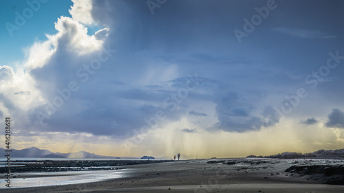 Padre e hijo pasean por una larga playa con gran cantidad de nubes sobre ellos mientras llueve photo