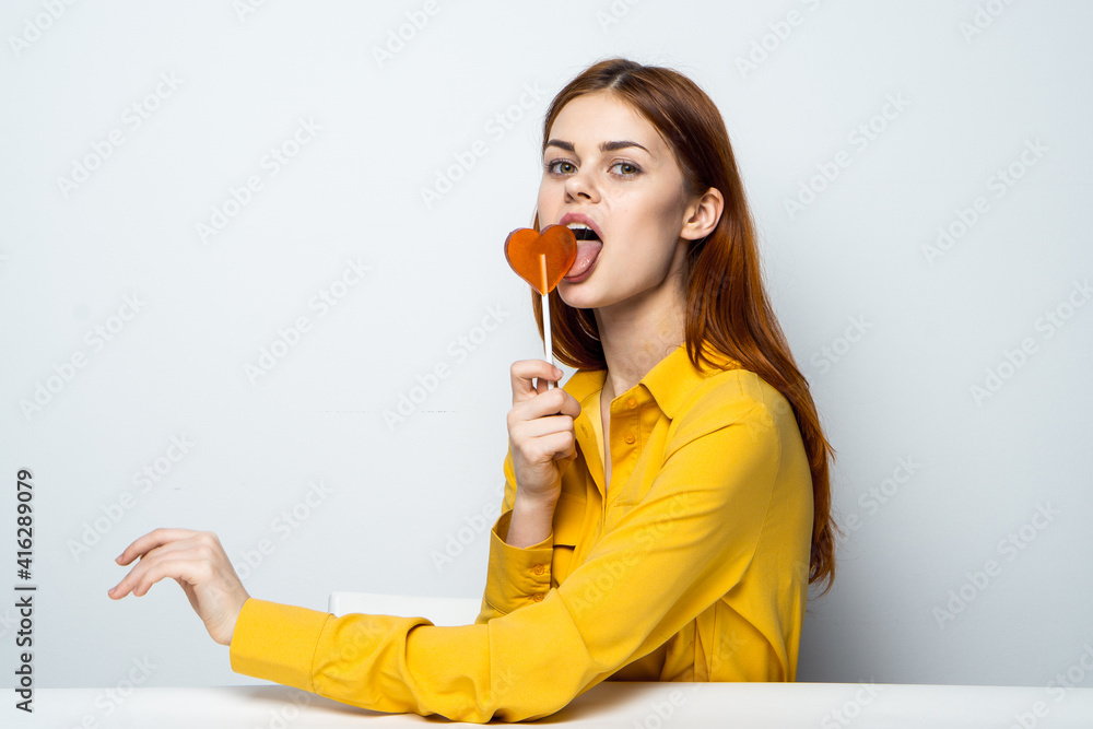 pretty woman with lollipop like in a yellow shirt sits at the table emotions pretty woman with lollipop like in a yellow shirt sits at the table emotions