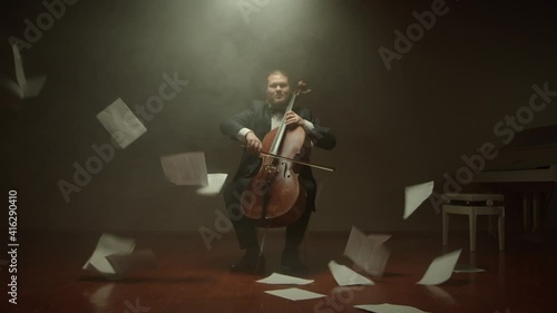 Cellist is playing his cello alone on stage,notes fall from the air