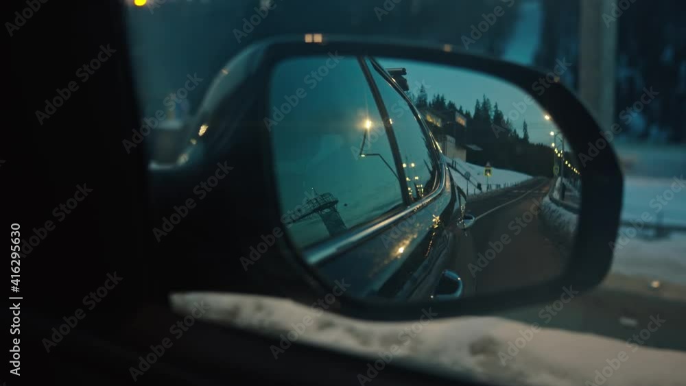 Car drive on highway in snowy landscape countryside. Close-up road to mountains reflecting in rear view car mirror. Ski resort. Winter roadtrip. Car drive on highway in snowy landscape countryside. Close-up road to mountains reflecting in rear view car mirror. Ski resort. Winter roadtrip.