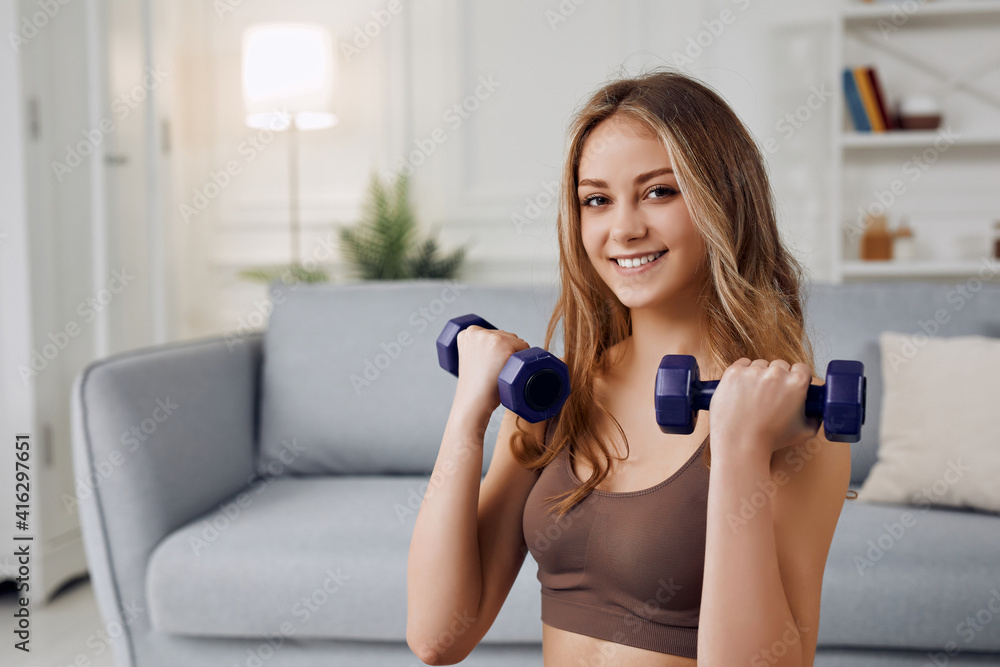 View of a young attractive girl doing exercise at home with dumbells. Healthy lifestyle.