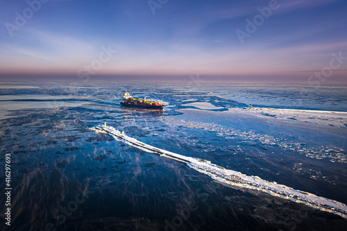 Obraz na płótnie Cargo ship driving through frozen sea with colorful containers. Dark waters with ice blocks floating in sea. w salonie