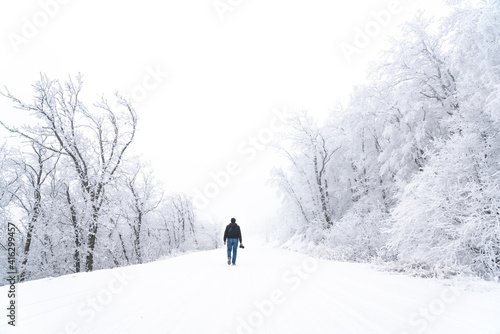 Travel photographer walking on a snowy road in the forest