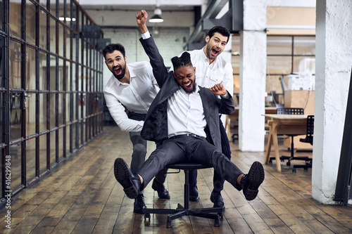 Work hard play hard. Four young cheerful business people in formal wear having fun while racing on office chairs and smiling.