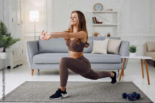 Young beautiful athletic girl in leggings and top makes lunges. Healthy lifestyle. Woman doing exercises at home.