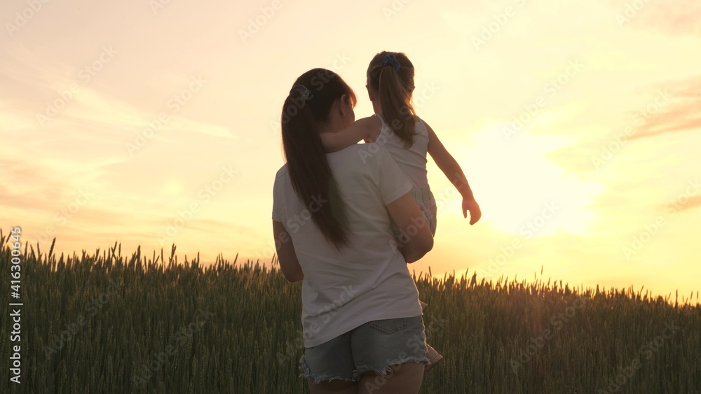 Mom and daughter walk past a wheat field and admire the sun's rays. Happy family mom and daughter in field at sunset. Mother farmer and child. The concept of happy family and being with nature