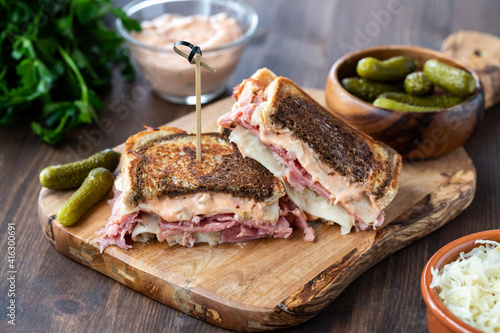 Close up of a toasted Reuben sandwich on a wooden board served with pickles, sauerkraut and Russian dressing.