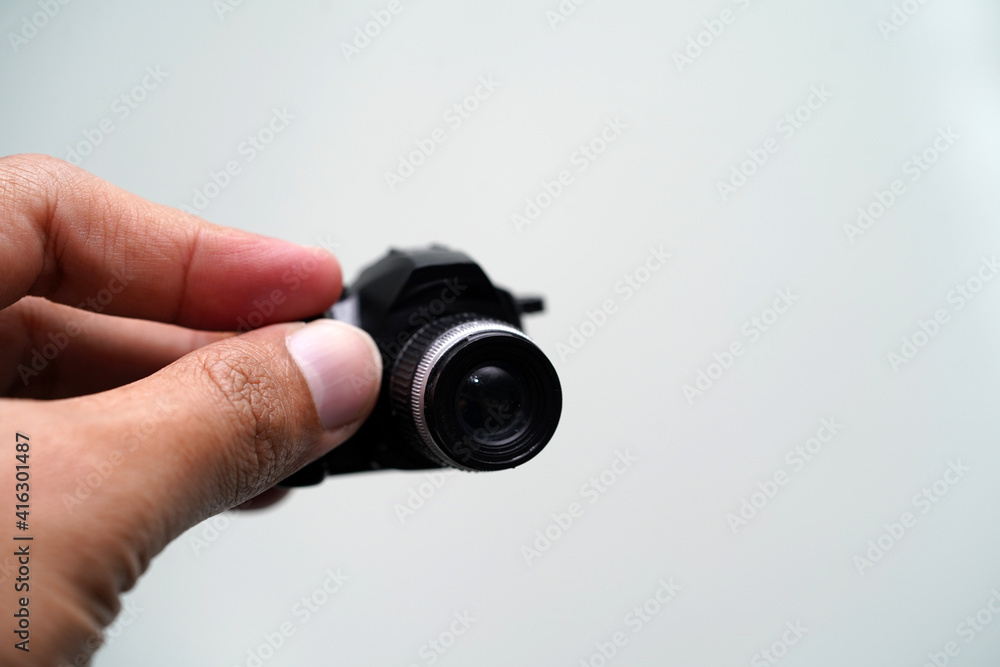 Hand holding mini fake camera isolated with light grey background, selective focus.