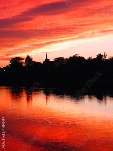 Red sunset over the river Maine with the silhouette of a church tower reflected in the water