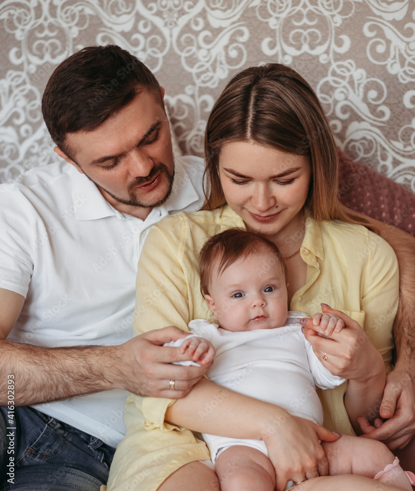 Young beautiful parents with newborn daughter in their arms look at the baby Young beautiful parents with newborn daughter in their arms look at the baby
