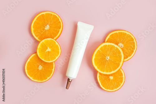 Top view of face and eye cream squeeze cosmetic tube with long nozzle and bronze screw cap and orange slices on powdery pink background. Stylish branding mockup, flat lay.