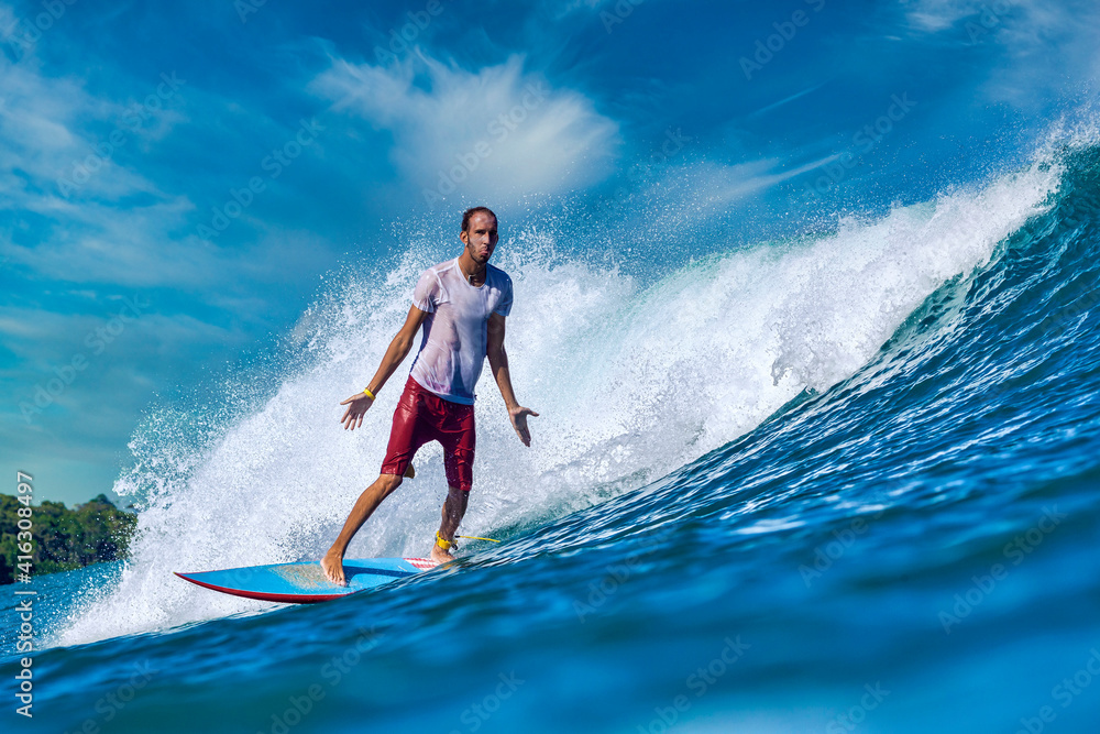 Male surfer on a blue wave at sunny day